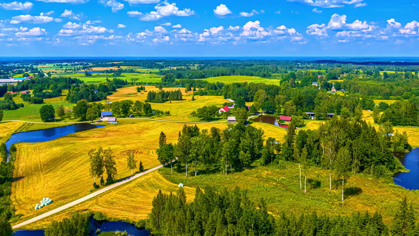 Picturesque ponds, farms, trees and fields of crops in a vibrant rural landscape in Europe under a fluffy cloudscape - aerial parallax hyper lapse