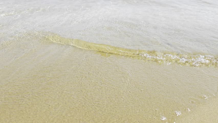 Calming waves on a sandy shore.  A video of gentle, lapping waves on a sandy beach, capturing the peaceful, rhythmic motion of the water and the soft texture of the wet sand.