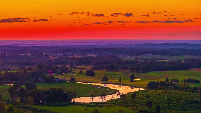 Sunset over patchwork farmland and winding country roads with warm orange reds reflected in water