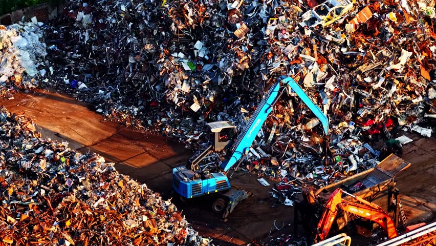 Excavator loading a crusher, shredder compactor at a metal recycling yard form a huge heap if scrap material - tilt down aerial