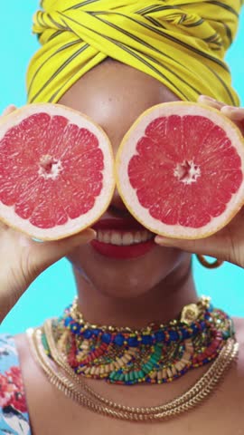 A Vibrant Woman Holding a Juicy Grapefruit, Adorned with Colorful Accessories and a Stylish Turban