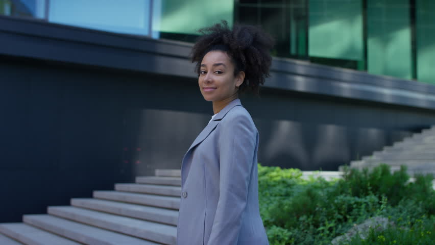 Portrait of a confident MBA student standing with arms crossed, smiling in front of a modern business school building.
