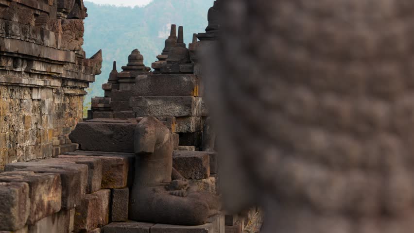 Left parallax glide at Borobudur reveals Buddha statues and relief carvings in shallow depth of field, highlighting ancient Buddhist architecture in Central Java, Indonesia
