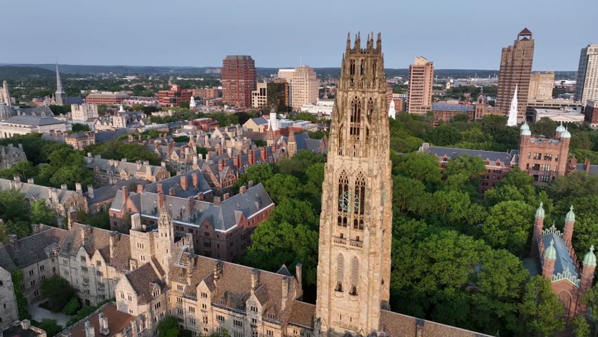 Harkness Tower at Yale old campus university of New Haven. American City in Connecticut at sunset. Summer day with green trees. Connecticut Financial Center In background. Aerial orbit wide shot.
