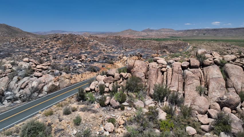 Aerial view of a long road cutting through a rocky desert landscape with contrasting burnt and untouched areas, Kirkland, Arizona, United States.