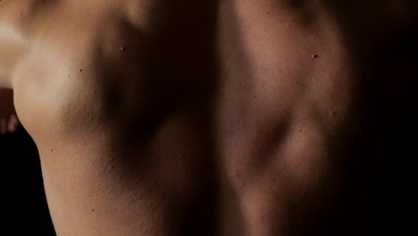 A bodybuilder uses the fly simulator to train his pectoral muscles. Upper body workout in a dark gym, view from the back. A handsome bodybuilder trains in the gym on the fly press simulator.