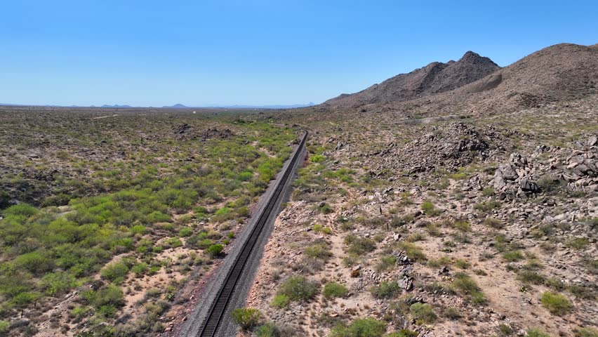 Aerial view of a single railroad track winding through the arid landscape, with sparse vegetation and rocky terrain, Congress, Arizona, United States.