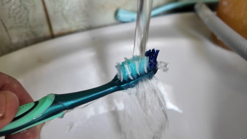 Toothbrush under running water. Close-up of a hand holding a toothbrush under running water. The hand carefully rinses the toothbrush from toothpaste residue, directing the flow of water from the tap.