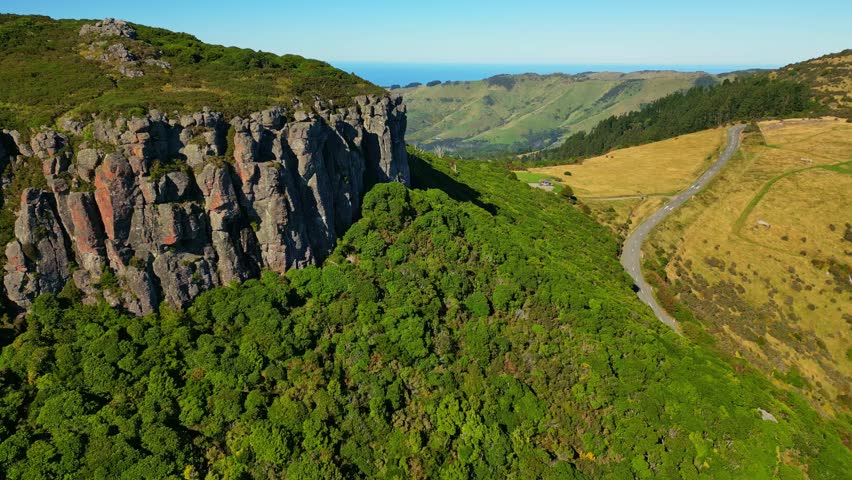 Aerial view of a rugged cliffside contrasting with the winding road and lush green hills, a blend of nature