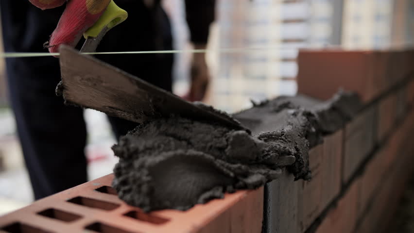 Builder laying bricks with mortar on construction site