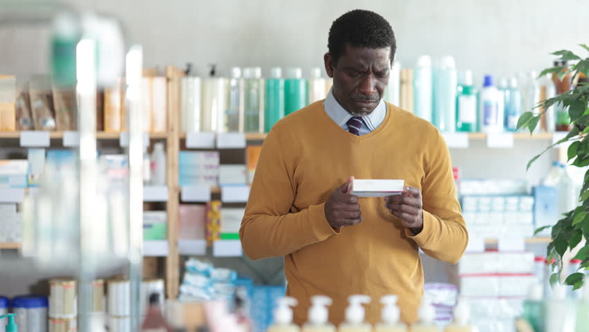 African man choose buy painkiller tablet at pharmacy, compare with other good.