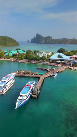 Aerial view of Tonsai Pier on Koh Phi Phi Don, Thailand, with ferries docked in turquoise waters, tropical coastline, and scenic limestone cliffs in the background.