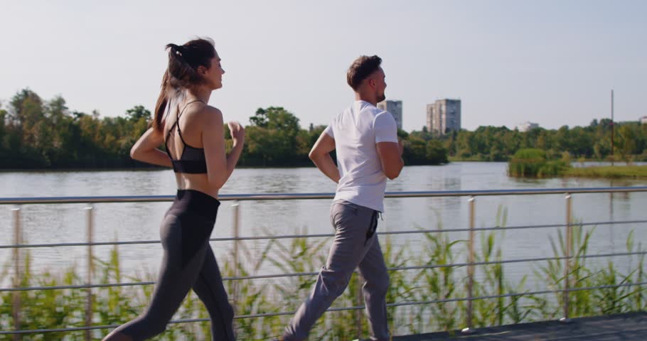 Active young happy couple in sportswear jogging together in the park during sport jog training. Man and woman running outdoors. Workout in nature and healthy lifestyle concept. 4k video. Slow motion.