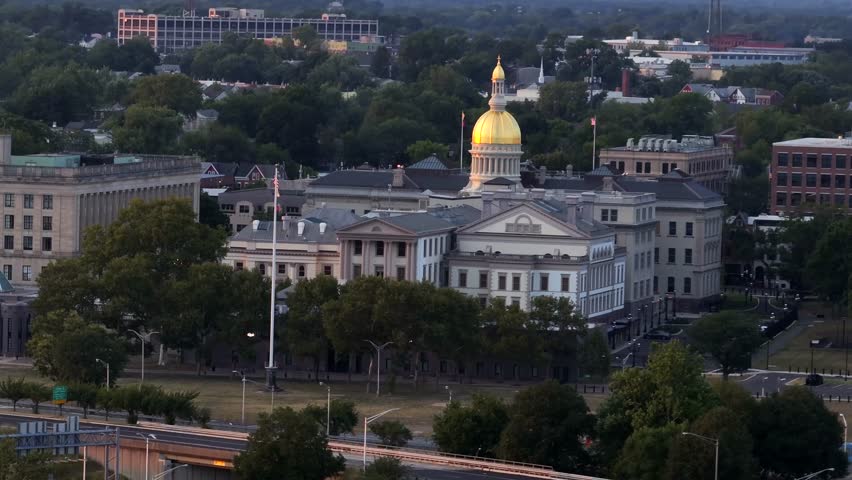 New Jersey State Capitol with golden cupola, with american flag ion flagpole in front yard. Dusk scene in Trenton, New Jersey. Aerial wide shot.