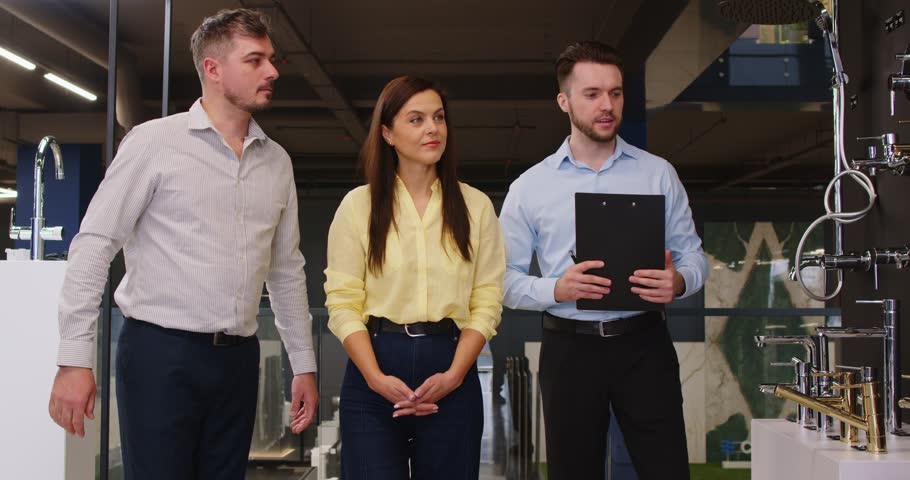 Couple with male salesman explores plumbing store, selecting shower or tap for home bathroom water needs, focusing on shop service in a professional setting with care and attention.