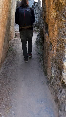 A young man walks through the ancient stone pathways of the Qenqo archaeological complex in Cusco, Peru. The footage captures the historic atmosphere and impressive stonework of the Inca ruins.
