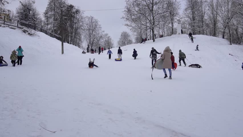 Children ride down a hill in winter on sleds and tubing, slow motion