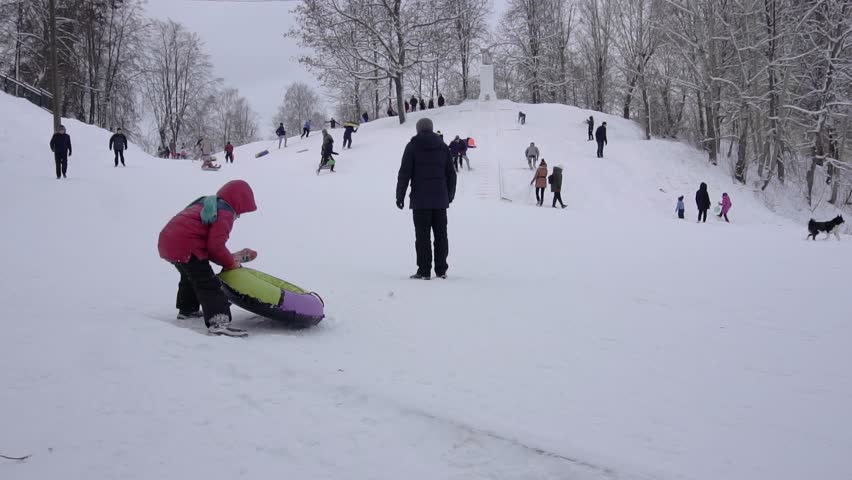 Children ride down a hill in winter on sleds and tubing, slow motion