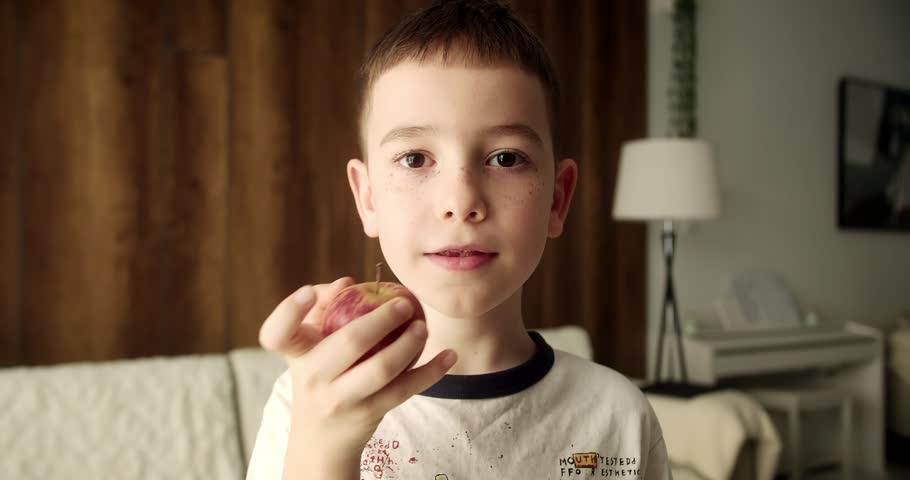 Close-up portrait of a child eating a ren apple. The camera focuses first on the child's face, and then on the hands with the apple.