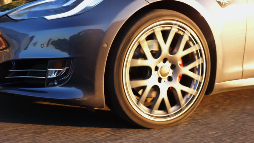 Wheel of modern electrical automobile driving at urban road on sunny day. Ecology friendly car riding moving along motorway. Electric vehicle riding through empty highway. Green innovation concept