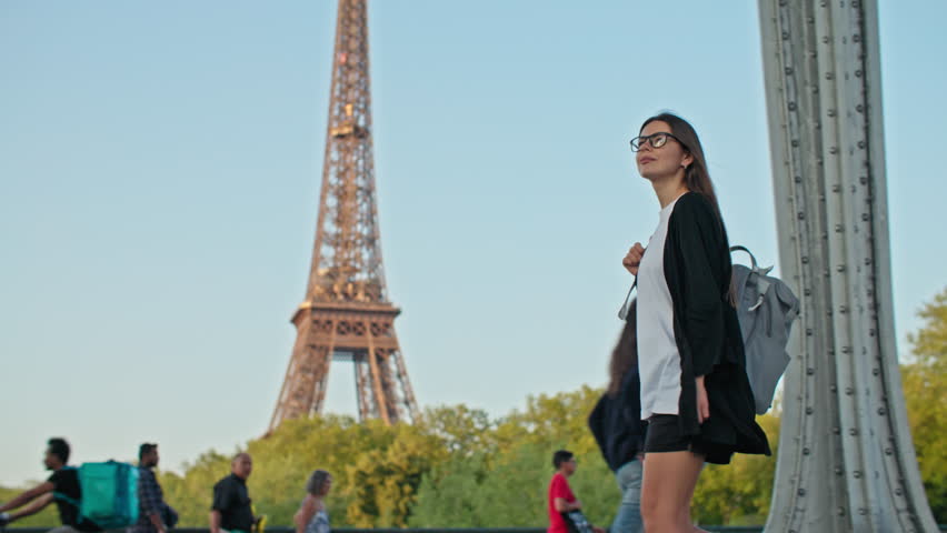 Happy tourist with backpack walking near the Eiffel Tower in Paris, France. Tourism and travel to the capital of France, beautiful landscapes and architecture in Europe.