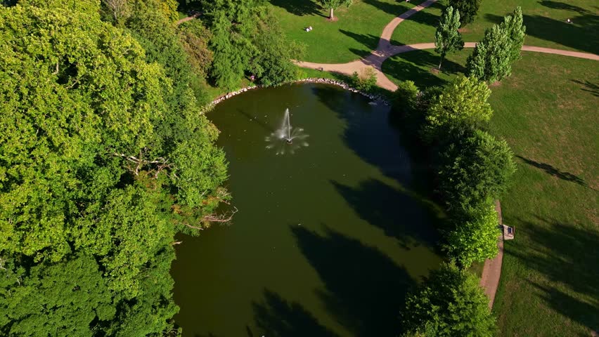 Tilt down drone movement over The Ondine Park aka Le Parc des Ondines' pond with water fountain in the middle, Changé, Mayenne, France.