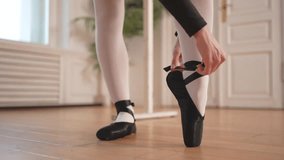 Ballerina puts on pointe shoes on leg in dance class. Classical ballet dancer woman in dance studio. Ballerina putting on tying classical pointe shoes for dance training. Ballet school concept - Powered by Shutterstock - Get 15% off with code: PIKWIZARD15