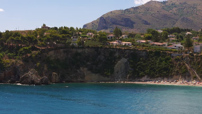Panning left aerial drone shot of coastal cliff at Guidaloca Beach (Spiaggia di Guidaloca) in Scopello, Sicily, Italy, during sunny Mediterranean summer travel