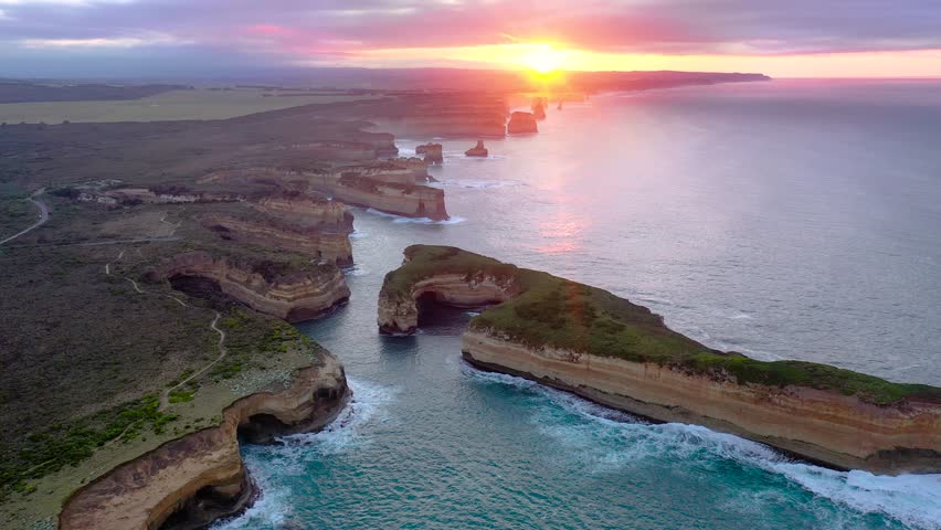 A drone view of the Twelve Apostles cliffs and ocean waves glowing under vibrant sunset skies on Australia southern coast