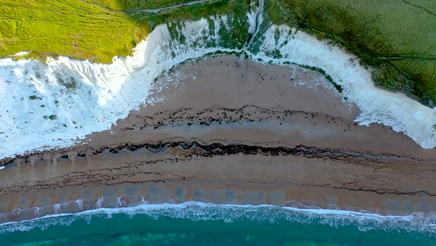 An aerial view of the Jurassic Coast white cliffs and layered rock formations meeting the sea in southern England