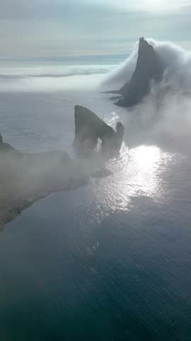 Experience the breathtaking cliffs of Drangarnir shrouded in mist, with stunning ocean reflections. The mysterious landscape captures the raw beauty of the Faroe Islands, offering serene vistas.