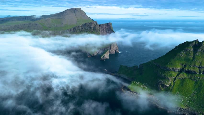 Majestic Drangarnir cliffs rise dramatically from the Atlantic, surrounded by mist and greenery. This stunning landscape showcases the raw beauty of the Faroe Islands and invites adventure seekers.