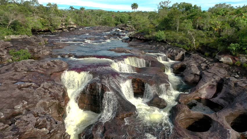 Colorful waters cascading through rocky formations in Colombia Cano Cristales River, creating a vibrant natural spectacle surrounded by lush jungle