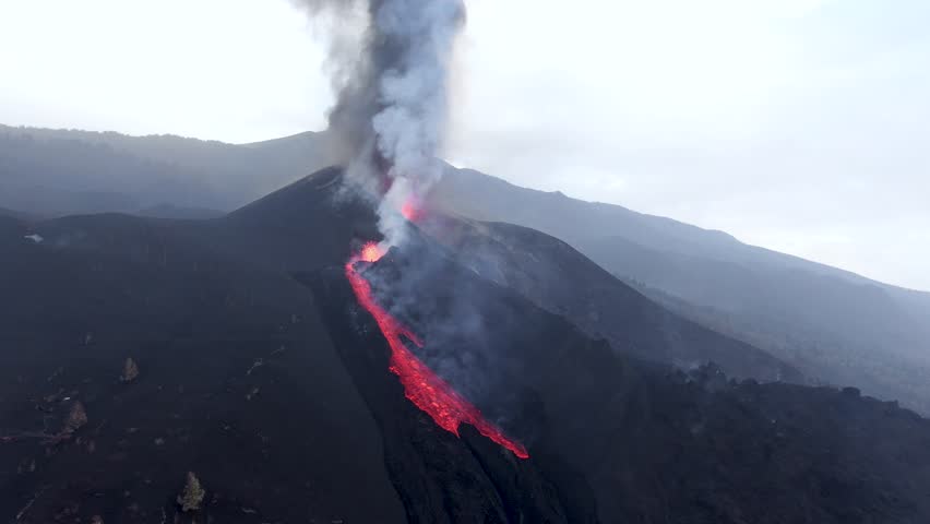 A drone view capturing glowing molten lava flowing down the slopes of the Cumbre Vieja volcano during an active eruption on La Palma, Spain