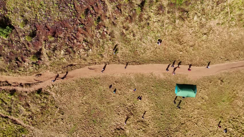 Aerial top-down view of hikers walking along a trail through dry grasslands. Mount Prau, Indonesia.