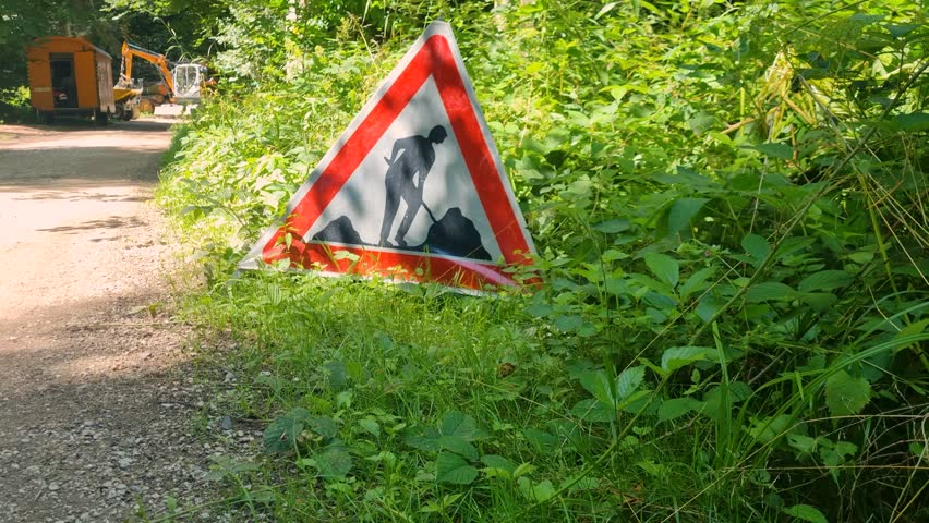 triangular warning sign in a Bern forest alerts pedestrians to forestry work, its vivid red contrasting with lush summer greenery in Switzerland