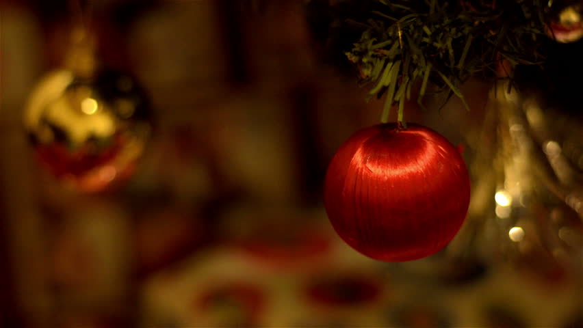 A red bauble ornament hanging on a Christmas tree, with other decorations in the