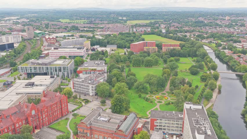 Aerial view over Salford Crescent showing the University of Salford campus, Peel Building, New Adelphi, Maxwell Building, Peel Park, student residences, and the River Irwell flowing alongside.