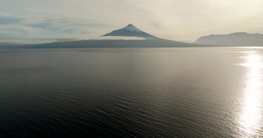 Lake Llanquihue towards majestic Osorno Volcano, snow-capped peak, sunlight reflects on water, Puerto Varas, Chile. Aerial forward, copy space