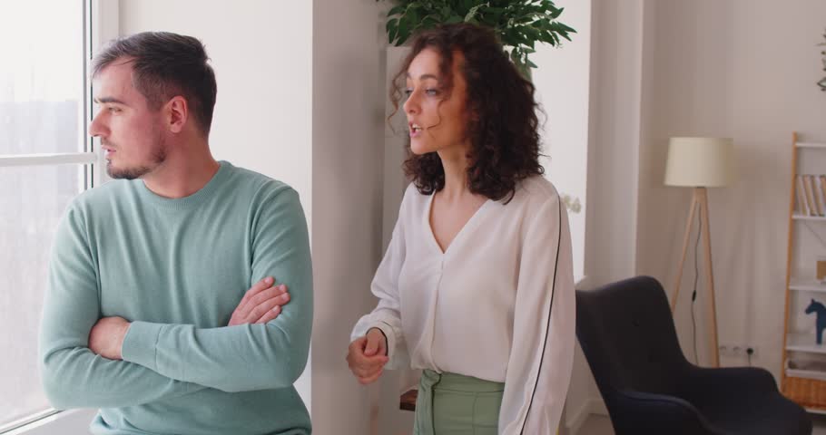 Young upset couple standing at home and arguing in quarrel. Unhappy husband and wife quarreling in the living room. Marriage problems, relationship and divorce concept. 4k video. Slow motion video.