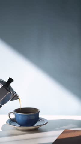 Pouring espresso coffee in a cup, morning coffee and breakfast concept, blue sunlit background with copyspace