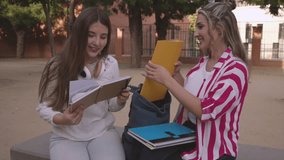 Two young women, likely university or high school students, sit on a bench outside, sharing notes and studying together, engaged in a lively discussion about their academic work - Powered by Shutterstock - Get 15% off with code: PIKWIZARD15