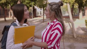 Female students sharing notes from yellow binder, walking together with arm around each other, displaying friendship and academic collaboration on sunny campus - Powered by Shutterstock - Get 15% off with code: PIKWIZARD15