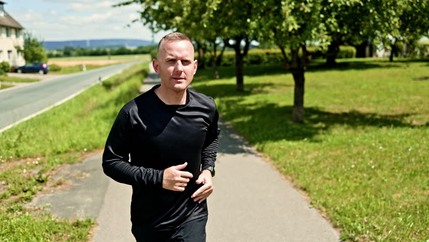 Athletic strong healthy man runner outdoors. Young guy on a morning jog on a sunny day. Cardio training outdoors. Healthy lifestyle. Man in black shorts and jersey.