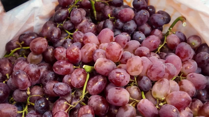 A person is holding a white plastic wrapped apple in a store. The pear are in a bin and are surrounded by plastic