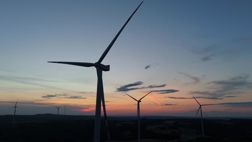Drone view of wind turbines on hillside at sunset, renewable energy powering sustainable countryside electricity.