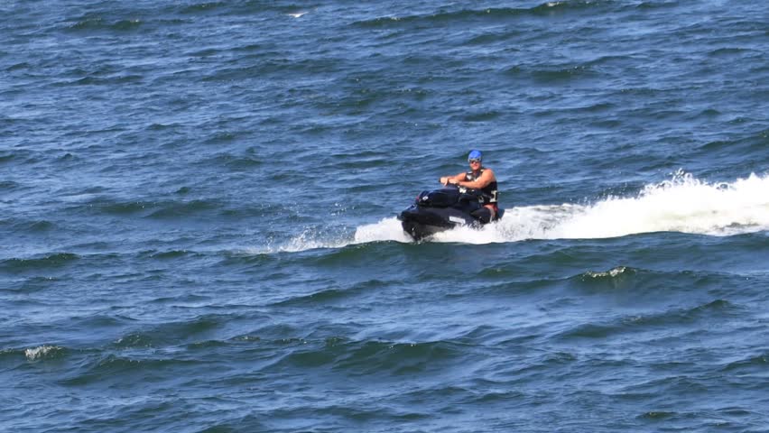 Man riding black jet ski over blue sea with splashing water under bright sunlight. Action shot capturing summer fun and speed on ocean waves.	