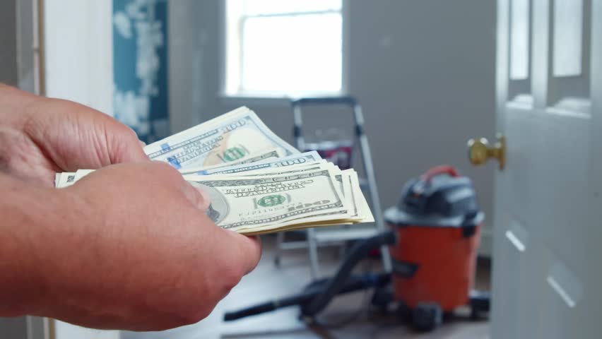 Counting Money In Renovated Space Full Of Painting. Modern Room Renovation Scene Where Man Handles Cash, Managing Budget, Surrounded By Construction Gear, Symbolizing Home Investment And DIY Spirit.