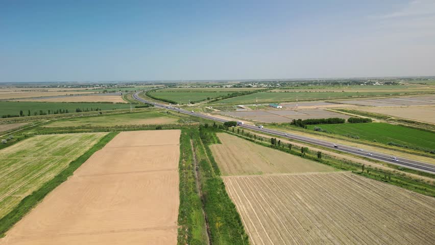 Wide-angle view of farmland, roads, and rural layout in Uzbekistan. Rich green fields and dry plots surround the curving highway under clear skies