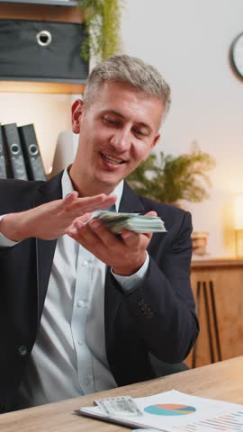 Cheerful rich Caucasian young freelancer man wasting throwing money dollar cash more tips earnings big profit success win lottery shopping. Happy handsome guy with laptop sitting at home office desk.